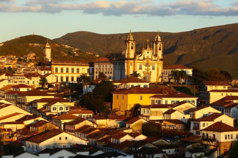 Vista panorâmica de Ouro Preto ao pôr do sol com igrejas coloniais em destaque e montanhas ao fundo